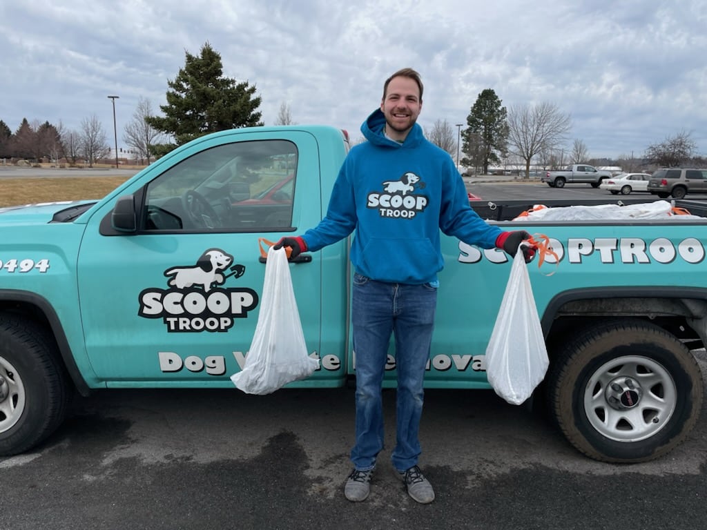Andrew from Scoop Troop holding bags of dog waste in front of a company truck.